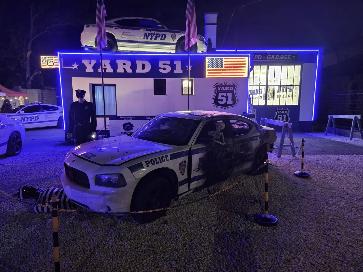 A YARD 51 épülete éjszaka kék neonfényben, előtte a kaszkadőr rendőrautó