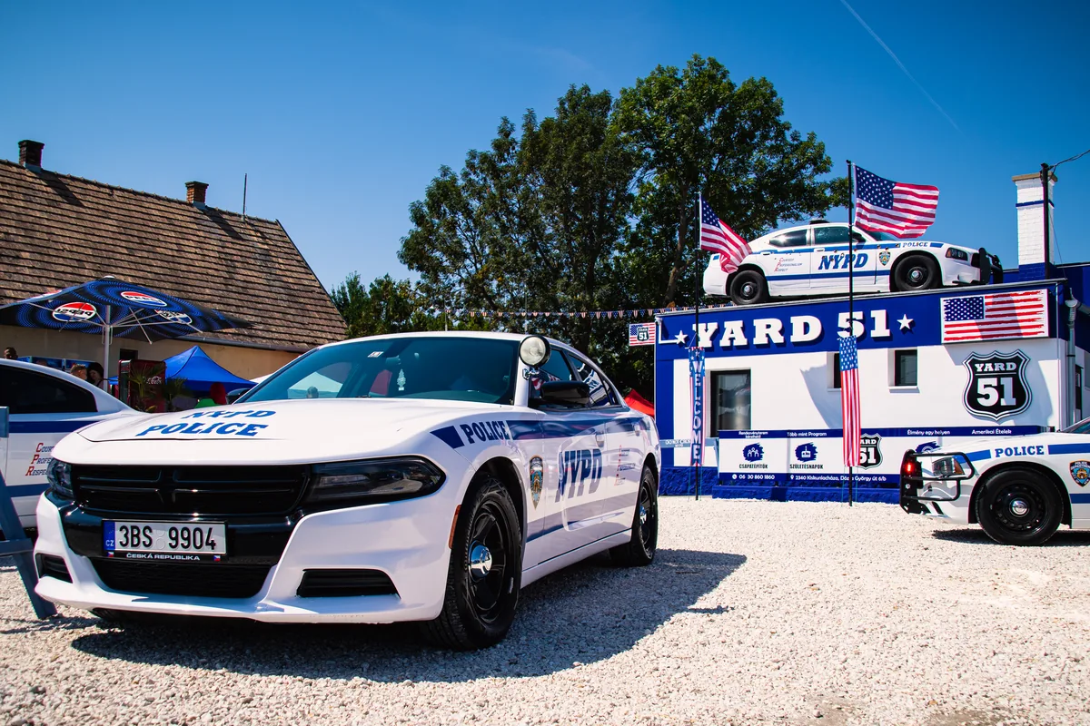 NYPD rendőrautó a YARD 51 udvarán, háttérben az épület és a napernyők