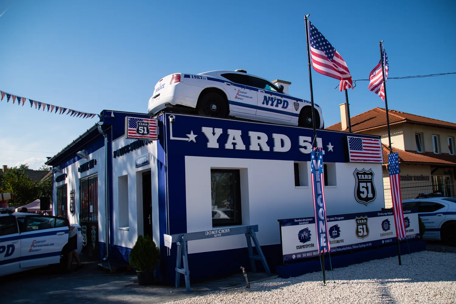 A YARD 51 épülete nappal, a tetején NYPD rendőrautóval, amerikai zászlókkal és a Yard 51 táblákkal